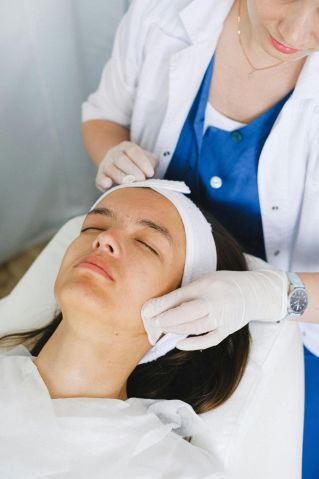 From above of crop anonymous cosmetologist in medical uniform cleaning face before facial procedure in beauty clinic
