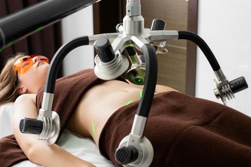 Female client lying on table under lasers of modern weight loss machine on belly during liposuction procedure in medical clinic