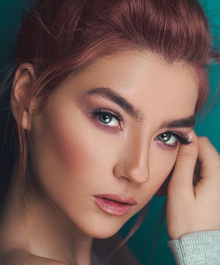 A fashionable adult woman posing with elegant makeup against a teal background.
